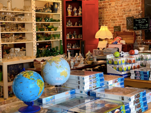 A cozy shop interior featuring globes, puzzles, and various collectibles on display against a brick wall.