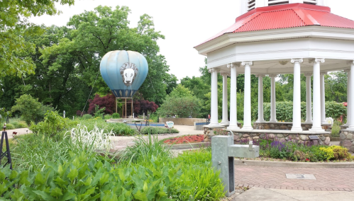 A colorful hot air balloon near a gazebo in a lush garden with vibrant flowers and greenery.