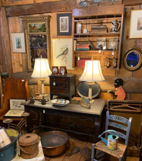A cozy antique shop display featuring lamps, framed art, and various vintage items on wooden shelves and furniture.