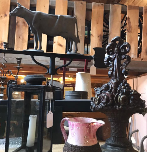 A collection of vintage items, including a metal cow figurine, a decorative urn, and various candle holders on display.