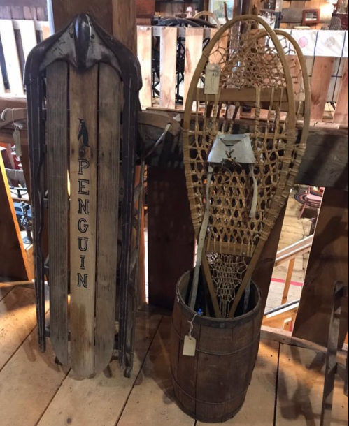 A wooden sled labeled "PENGUIN" next to a vintage snowshoe displayed in a rustic wooden setting.