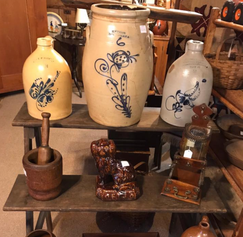 A display of vintage pottery and wooden items, including jars, a mortar, and a decorative figurine on wooden shelves.