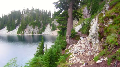 A serene lake surrounded by rocky terrain and lush evergreen trees under a cloudy sky.
