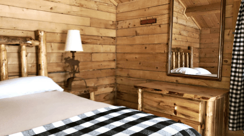Cozy wooden cabin interior featuring a bed, mirror, and rustic furniture with a checkered blanket.