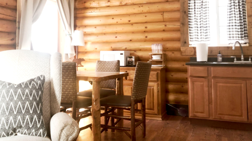 Cozy cabin interior with wooden walls, a dining table, chairs, and a kitchenette featuring a microwave and sink.