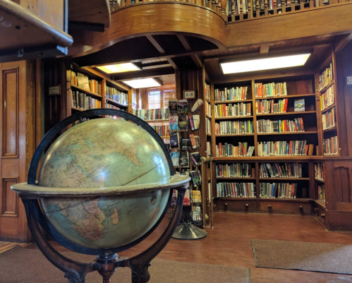 A vintage globe in the foreground with wooden bookshelves filled with books in a cozy library setting.
