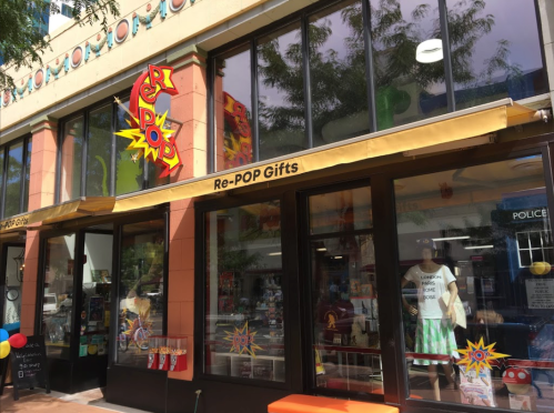 Storefront of Re-POP Gifts featuring colorful signage and displays, with trees and a street visible in the background.