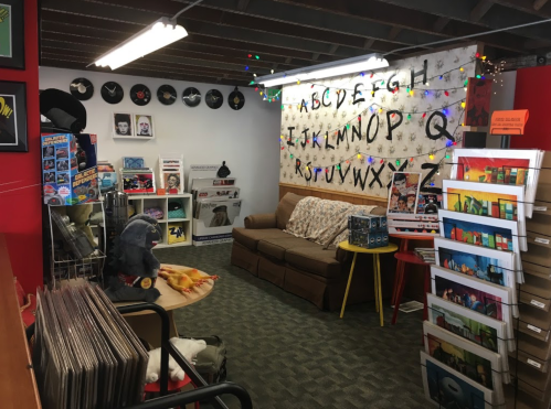 Cozy room with a couch, vinyl records, colorful lights, and a wall decorated with letters and artwork.