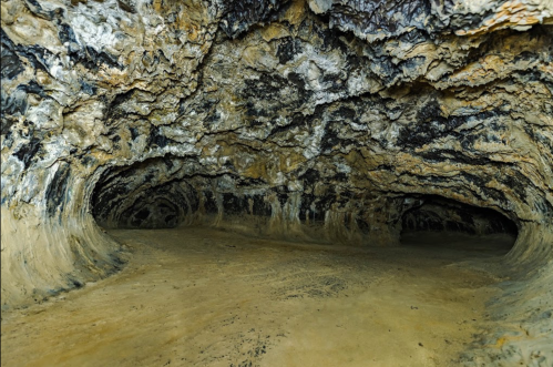 A dark cave interior with textured rock formations and a sandy floor, creating a mysterious underground atmosphere.