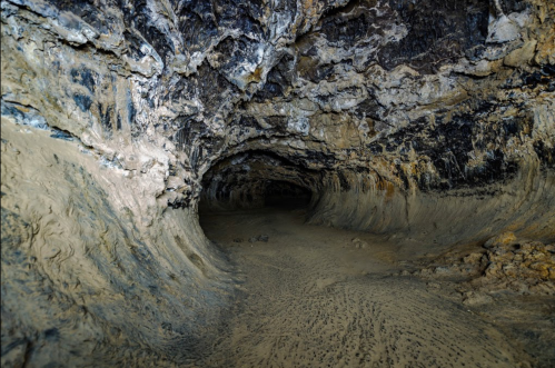 A dark, winding cave with textured walls and a sandy floor, illuminated by soft light.