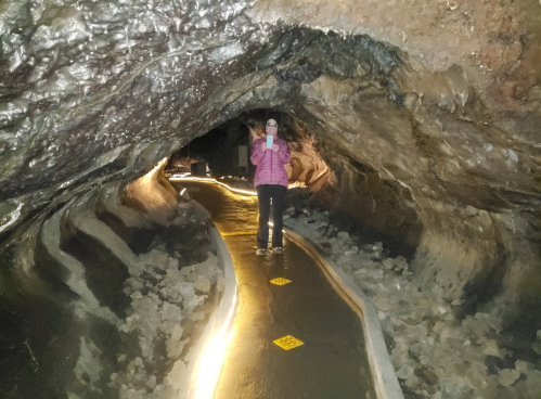 A person stands on a lit path inside a cave, surrounded by rocky walls and mineral formations.