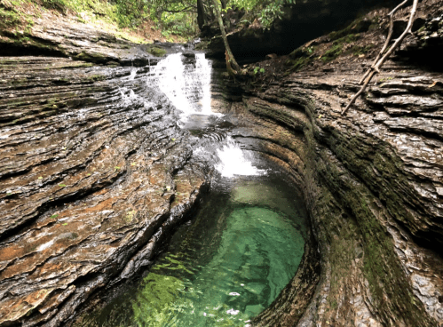 A serene natural scene featuring a small waterfall cascading into a clear, green pool surrounded by rocky formations.