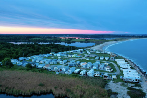Aerial view of a coastal campground at dusk, with trailers and a beach along the shoreline.