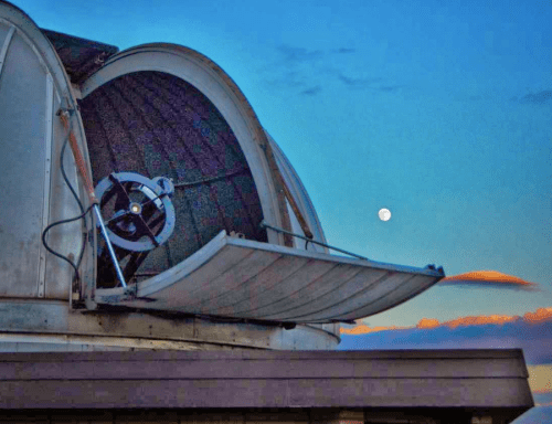 A telescope dome opens against a twilight sky, with a bright moon visible in the background.