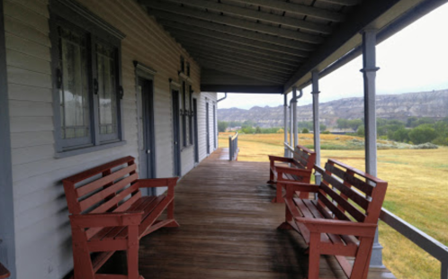 A porch with red benches overlooks a grassy field and distant hills under a cloudy sky.