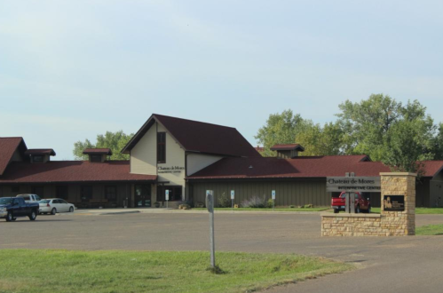 A building with a red roof and sign for "Charter de Mois" in a rural setting, surrounded by trees and a parking area.