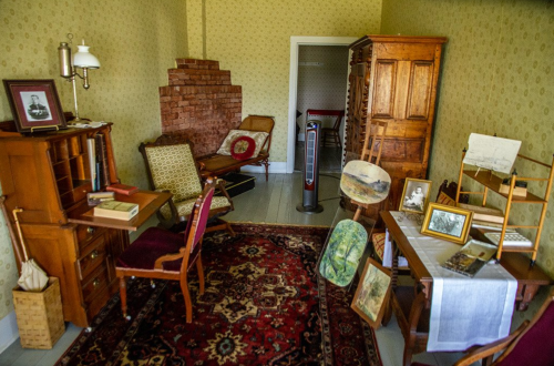 A vintage room with wooden furniture, a patterned rug, and various framed artworks on display.