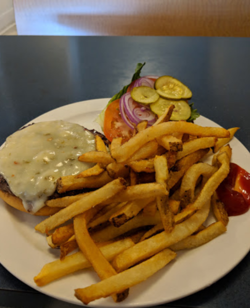A plate with a cheeseburger topped with lettuce, tomato, onion, pickles, and a side of golden French fries and ketchup.