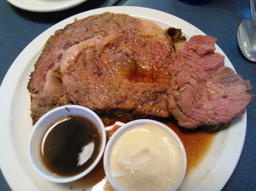 A plate of juicy prime rib served with two dipping sauces: a dark gravy and a creamy sauce.