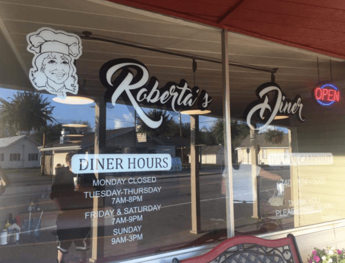 Exterior of Roberta's Diner with hours displayed, featuring a smiling chef logo and an "Open" sign.