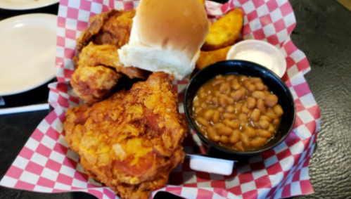 A basket of fried chicken, a bun, potato wedges, and a side of baked beans on a checkered paper.