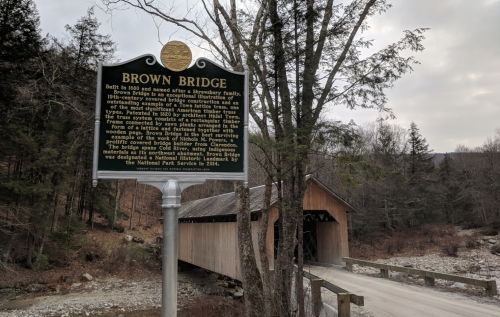 Historic sign for Brown Bridge, built in 1840, detailing its history and significance in the area. Surrounded by trees.