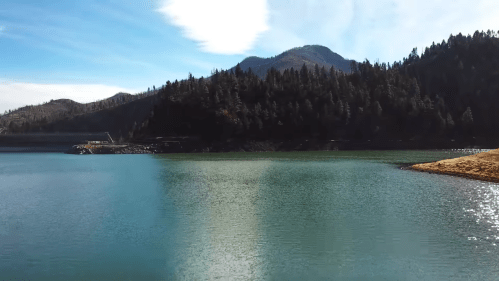 A serene lake surrounded by mountains and lush trees under a clear blue sky.