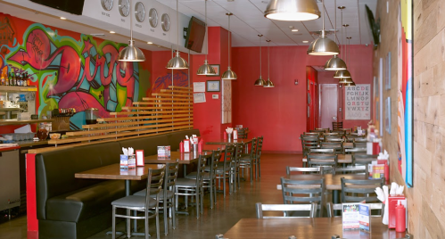 A vibrant restaurant interior with colorful graffiti, wooden accents, and empty tables ready for diners.