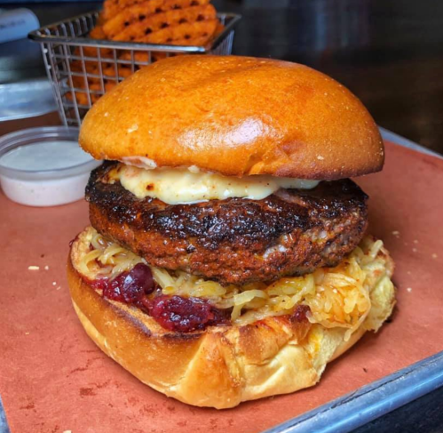 A close-up of a burger with a thick patty, melted cheese, sauerkraut, and a glossy bun, served with waffle fries.