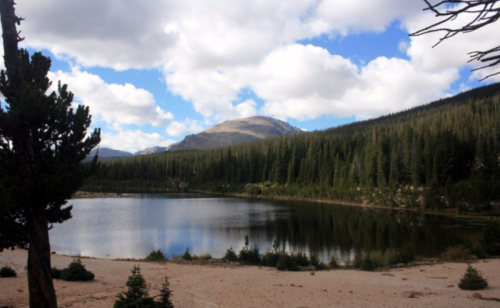 A serene lake surrounded by lush forests and mountains under a partly cloudy sky.