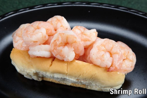 A shrimp roll featuring several pink shrimp on a soft bun, served on a black plate.