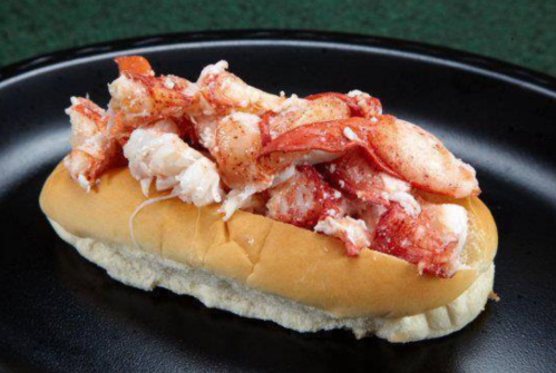 A lobster roll on a black plate, filled with chunks of lobster meat and a light seasoning on a soft bun.
