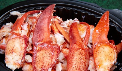 A close-up of cooked lobster claws, showcasing their bright red color and tender meat in a black container.