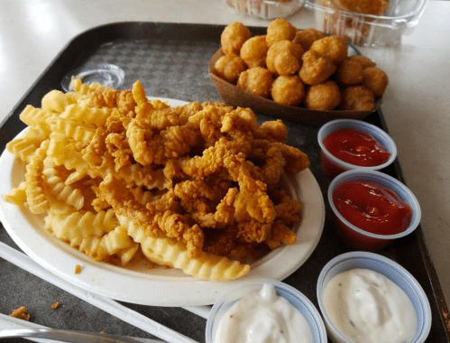 A plate of crispy fried chicken strips with crinkle-cut fries, served with ketchup and dipping sauces on a tray.