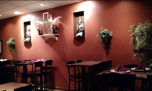 Cozy restaurant interior with red walls, decorative plants, and tables set with maroon napkins.