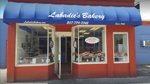 Exterior of Labadie's Bakery, featuring a blue awning, open sign, and display of baked goods in the windows.