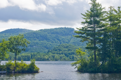 A serene lake surrounded by lush green hills and trees under a partly cloudy sky.