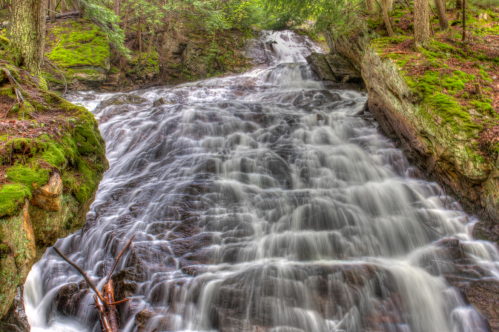 A serene waterfall cascading over moss-covered rocks in a lush, green forest.