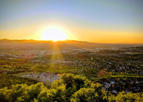 A stunning sunset over a valley, with mountains in the distance and a cityscape below, bathed in warm golden light.