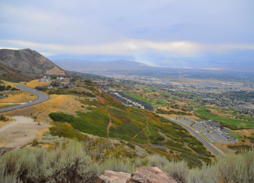 A scenic view of rolling hills and a valley, with winding roads and a mix of green and autumn-colored foliage.