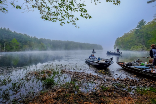 A misty lake scene with fishermen in boats, surrounded by lush greenery and foggy hills in the background.