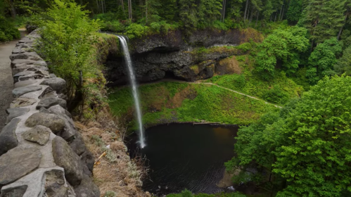 A scenic view of a waterfall cascading into a dark pool, surrounded by lush green trees and rocky cliffs.