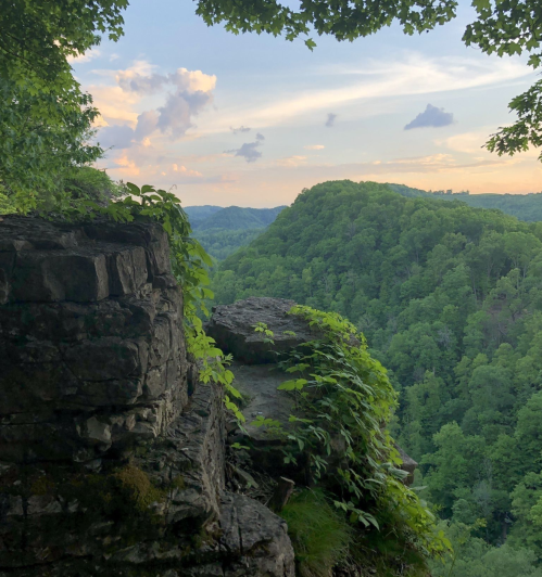 A scenic view of lush green hills under a colorful sky, with rocky outcrops in the foreground.