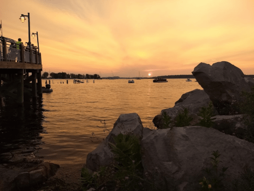 A serene sunset over a calm lake, with silhouettes of rocks and a pier in the foreground.