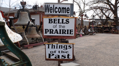 A sign with three sections: "Welcome," "BELLS of the PRAIRIE," and "Things of the Past," surrounded by vintage items.