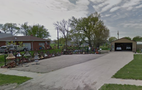 A residential area with a yard filled with various items and a garage, under a partly cloudy sky.