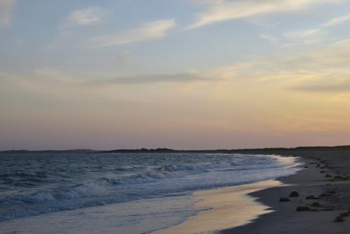 A serene beach at sunset, with gentle waves lapping at the shore and a colorful sky in the background.