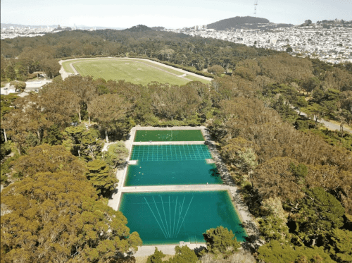 Aerial view of a park with two large, blue water features surrounded by trees and a grassy field in the background.