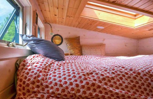 Cozy loft bedroom with a skylight, featuring a patterned duvet and pillows against wooden walls.