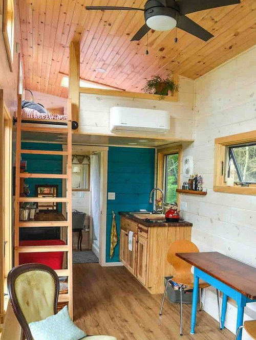Cozy tiny house interior featuring a loft, wooden accents, a kitchen, and a small dining area with a blue wall.